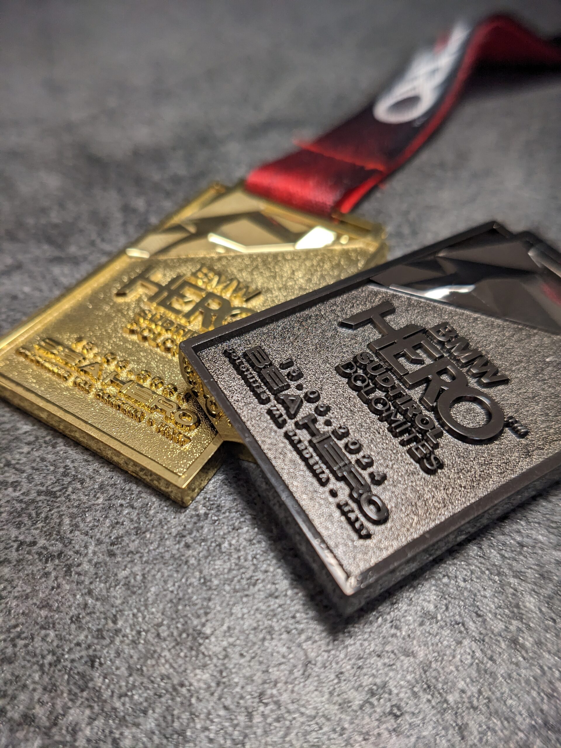 medaglia personalizzata hero in metallo a rilievo 3D senza smalti finitura oro e nichel nero con fondo satinato e rilievi lucidi con nastro personalizzato in sublimazione medaglia personalizzata hero in metallo a rilievo 3D senza smalti finitura oro e nichel nero con fondo satinato e rilievi lucidi con nastro personalizzato in sublimazione